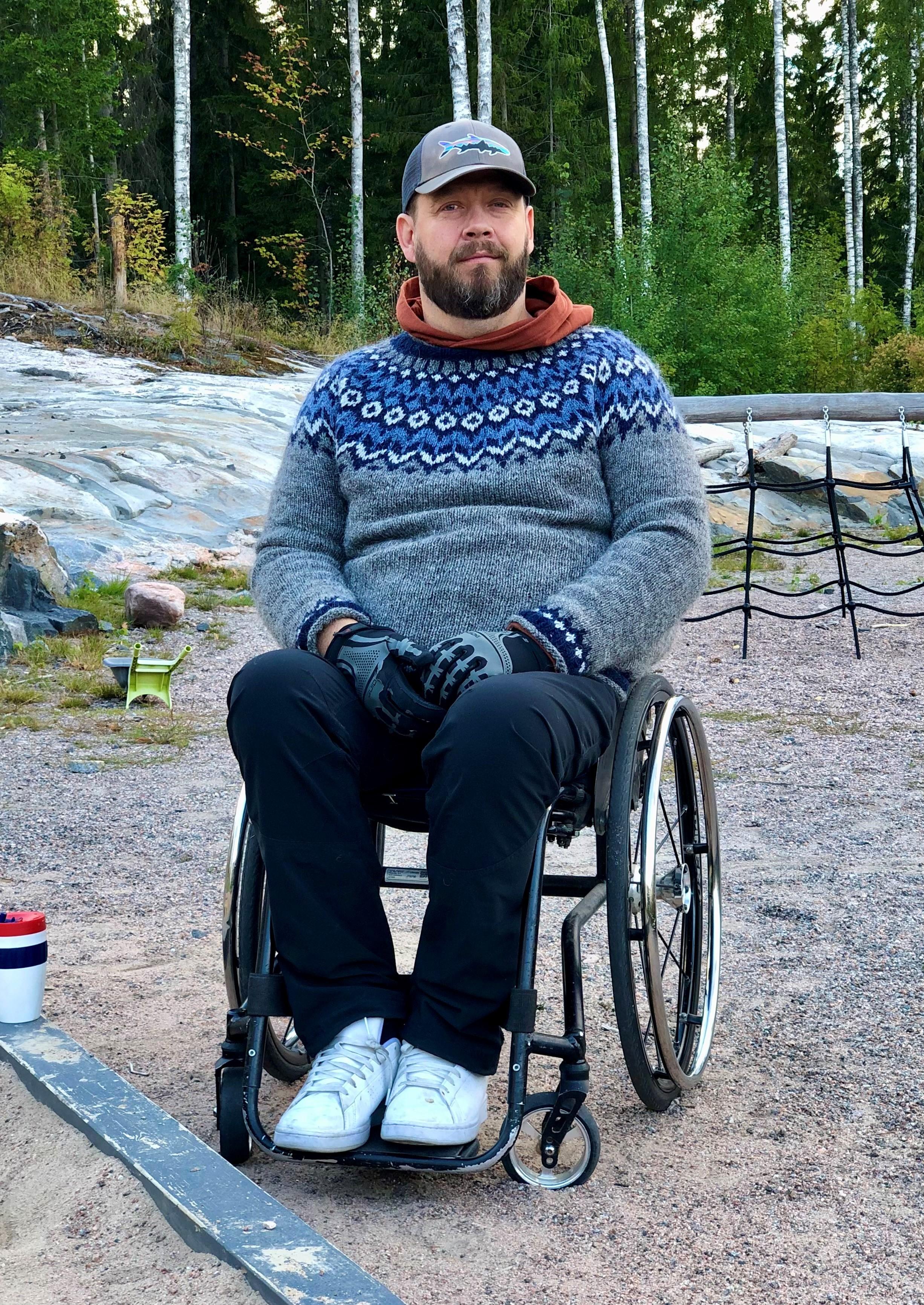 Jukka kuvattuna pyörtätuolissaan luontoympäristössä. Jukalla on päällä sini-harmaa kaarrokevillapaita.