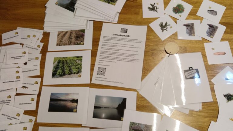 Pöydällä kortteja ja luontokuvia. Kannessa lukee Luontokapsäkki.